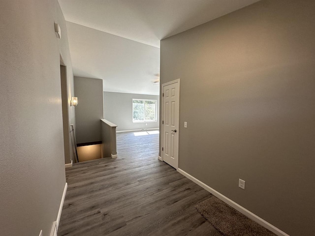 hall featuring lofted ceiling, baseboards, dark wood finished floors, and an upstairs landing