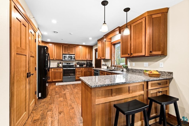 kitchen with dark stone counters, hardwood / wood-style flooring, a breakfast bar area, kitchen peninsula, and black appliances