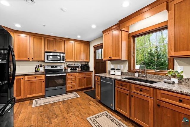 kitchen with stainless steel appliances, light stone counters, wood-type flooring, and sink