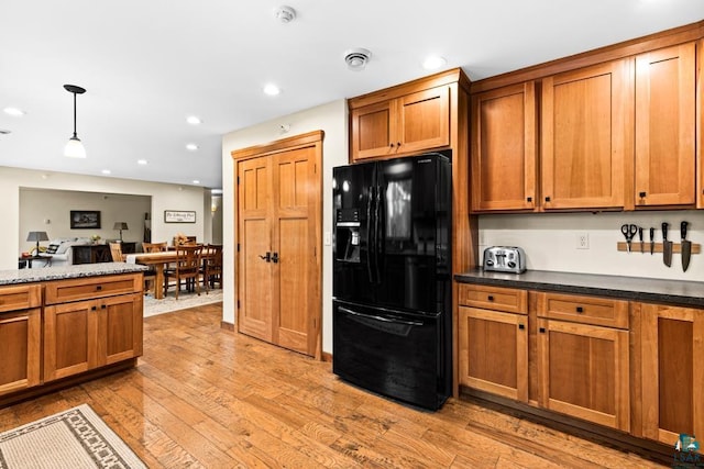 kitchen featuring light wood-type flooring, dark stone countertops, decorative light fixtures, and black refrigerator with ice dispenser