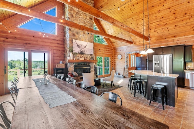 tiled dining space featuring wooden walls, a stone fireplace, beam ceiling, and high vaulted ceiling