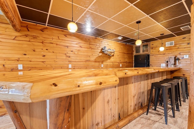 bar with hanging light fixtures, wood walls, butcher block counters, and black fridge