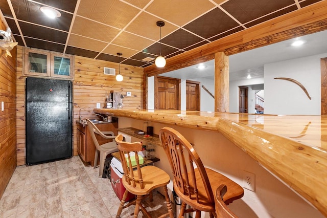 bar featuring butcher block counters, wood walls, and black refrigerator