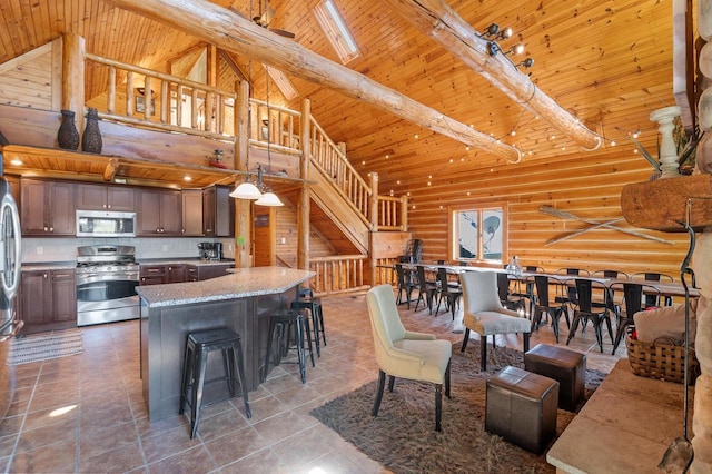 kitchen with beam ceiling, a kitchen island, high vaulted ceiling, log walls, and appliances with stainless steel finishes