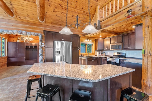 kitchen featuring appliances with stainless steel finishes, hanging light fixtures, light stone countertops, wooden walls, and sink