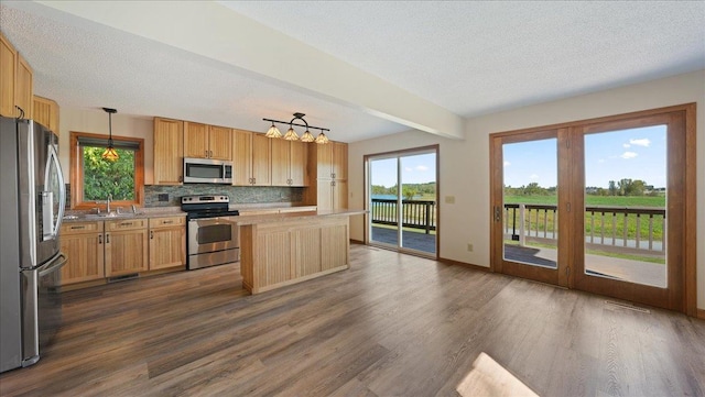 kitchen featuring appliances with stainless steel finishes, hanging light fixtures, tasteful backsplash, a kitchen island, and dark hardwood / wood-style flooring