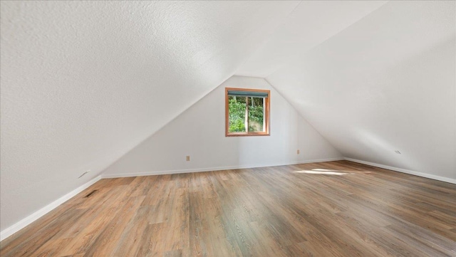 additional living space featuring vaulted ceiling, a textured ceiling, and hardwood / wood-style flooring