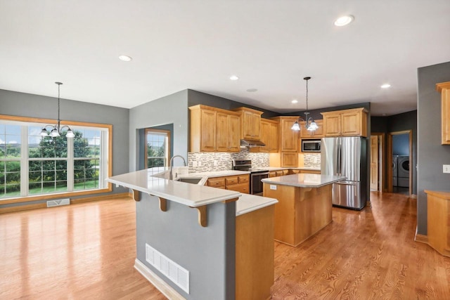 kitchen featuring sink, kitchen peninsula, stainless steel appliances, an inviting chandelier, and a breakfast bar area