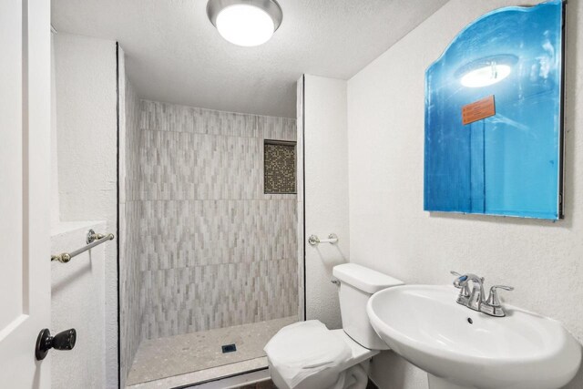 bathroom with a tile shower, sink, a textured ceiling, and toilet