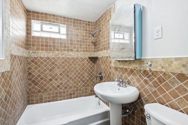 bathroom with tile walls, toilet, and tiled shower / bath combo