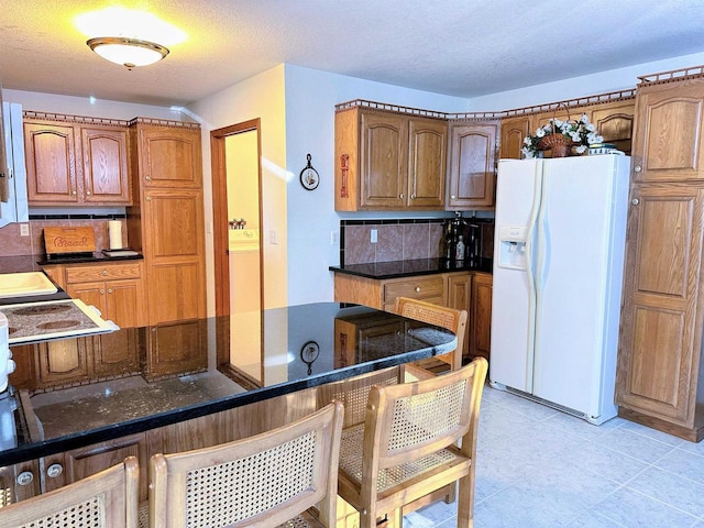 63574 Lohmann Ln, Eastman, WI 52626 - kitchen with white refrigerator with ice dispenser, a breakfast bar, backsplash, brown cabinetry, and a peninsula