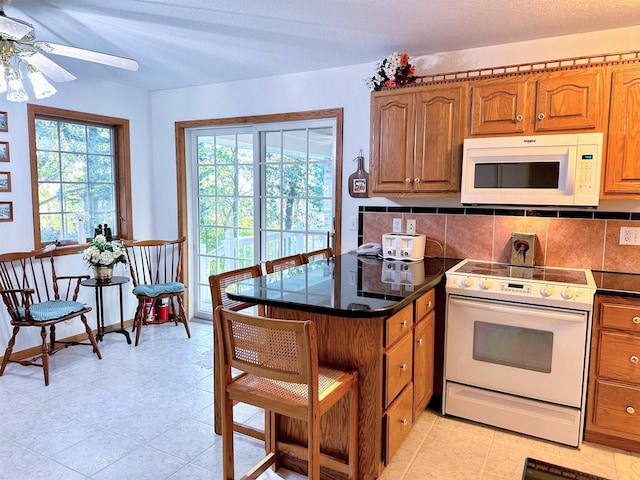 63574 Lohmann Ln, Eastman, WI 52626 - kitchen with white appliances, brown cabinets, ceiling fan, decorative backsplash, and dark countertops