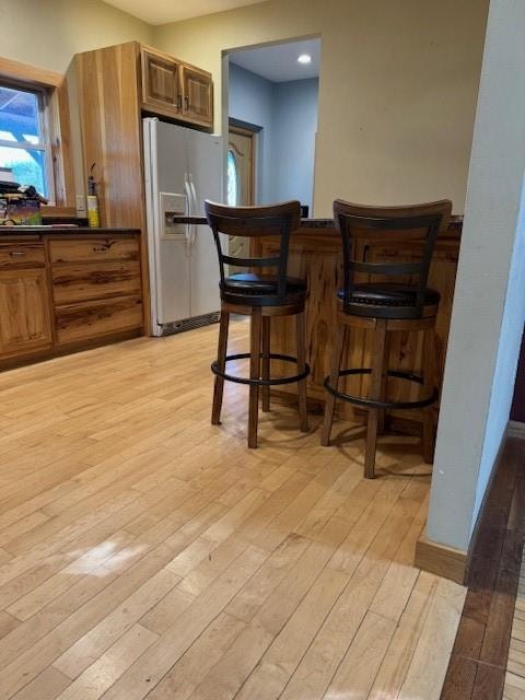 kitchen with white fridge with ice dispenser, light hardwood / wood-style flooring, and a breakfast bar