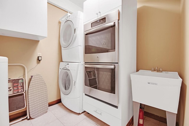 washroom with stacked washer / drying machine, sink, light tile patterned floors, and cabinets