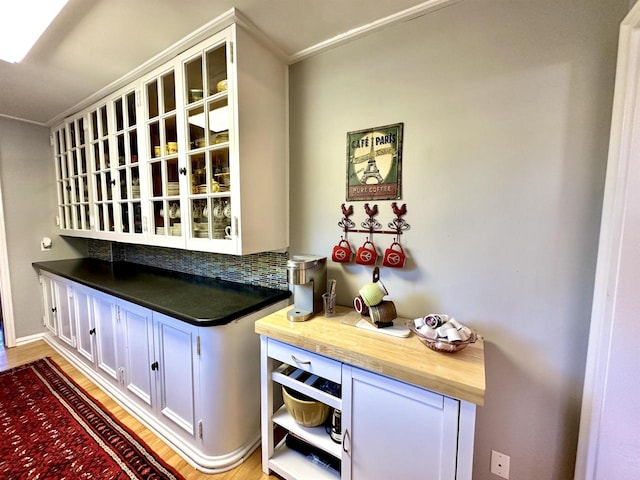 bar featuring decorative backsplash, crown molding, light hardwood / wood-style flooring, and white cabinets