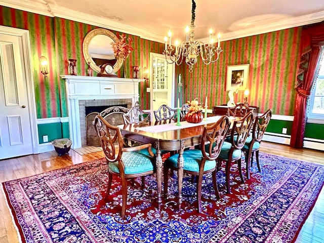 dining room with a brick fireplace, hardwood / wood-style flooring, ornamental molding, baseboard heating, and a notable chandelier