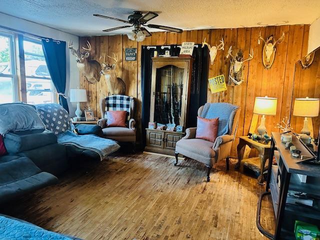 living room with wood-type flooring, a textured ceiling, wood walls, and ceiling fan