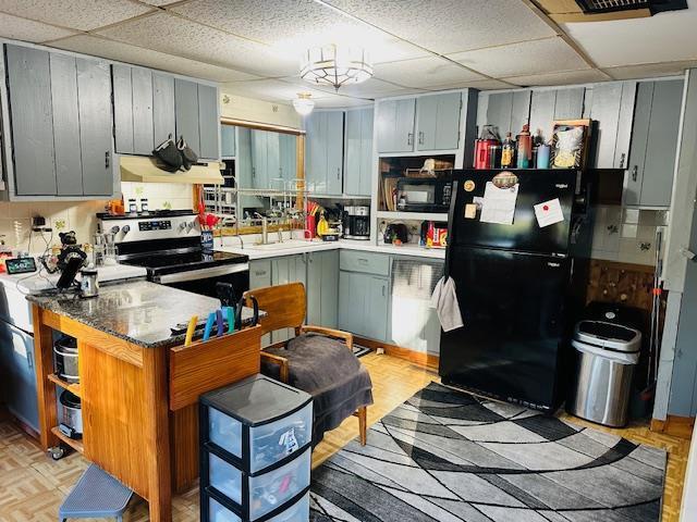 kitchen featuring a paneled ceiling, sink, black fridge, stainless steel electric range oven, and range hood