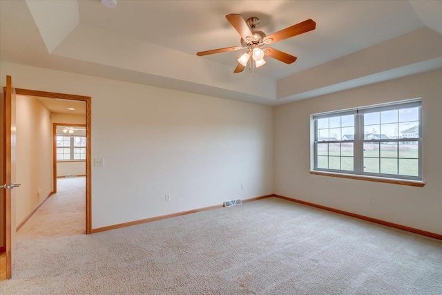 empty room with ceiling fan, plenty of natural light, light carpet, and a tray ceiling