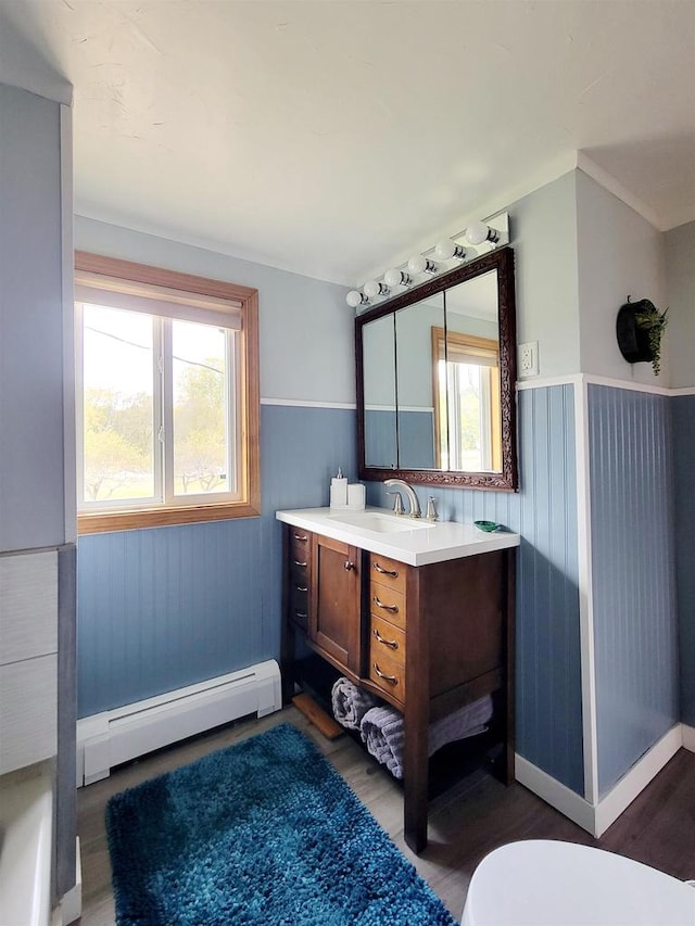 bathroom with toilet, wooden walls, a baseboard radiator, hardwood / wood-style floors, and vanity