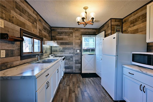 kitchen featuring wooden walls, white appliances, hanging light fixtures, and white cabinets