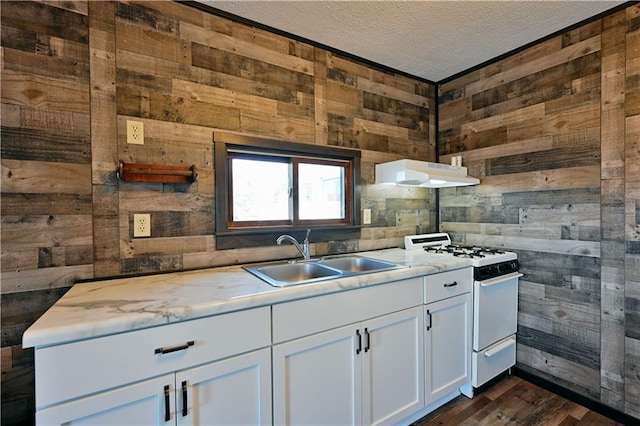 kitchen featuring white gas stove, wooden walls, white cabinetry, and sink