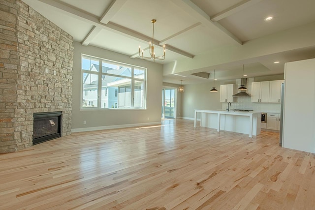 unfurnished living room with a notable chandelier, a stone fireplace, sink, and light hardwood / wood-style flooring