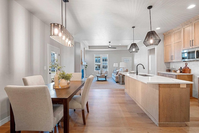 kitchen with light brown cabinetry, a center island with sink, hanging light fixtures, and light hardwood / wood-style flooring