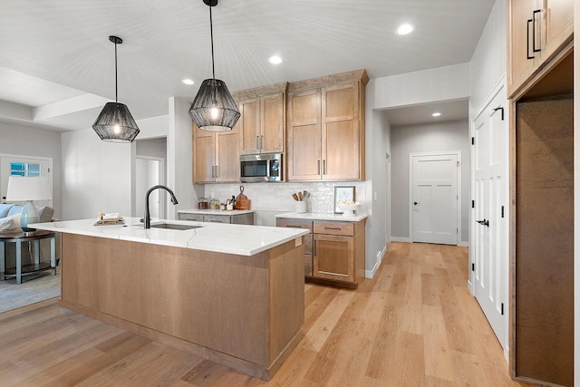 kitchen with an island with sink, hanging light fixtures, sink, and light hardwood / wood-style flooring