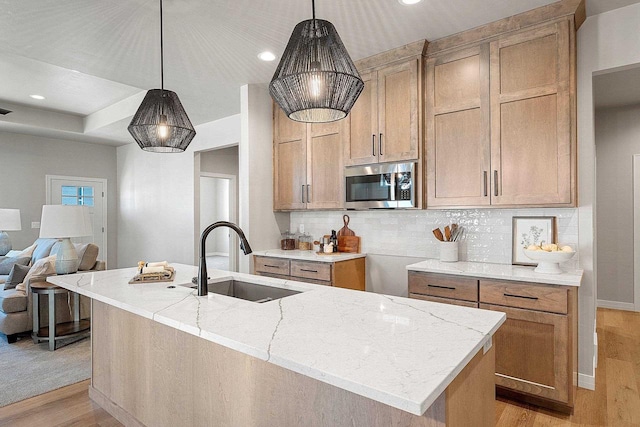 kitchen featuring an island with sink, pendant lighting, sink, and light hardwood / wood-style flooring