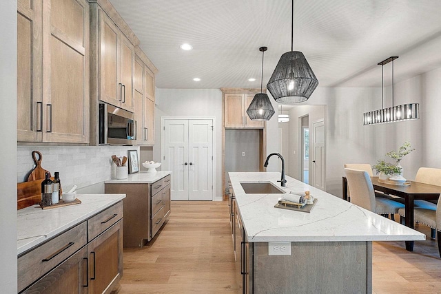 kitchen featuring light stone counters, sink, decorative light fixtures, a center island with sink, and light hardwood / wood-style flooring