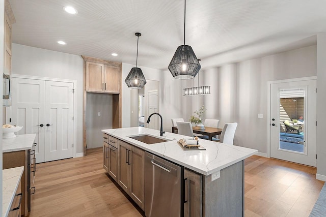 kitchen with light wood-type flooring, sink, hanging light fixtures, an island with sink, and stainless steel dishwasher