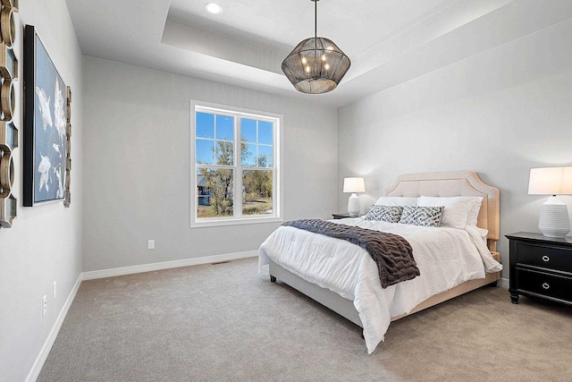 carpeted bedroom featuring a tray ceiling and a chandelier