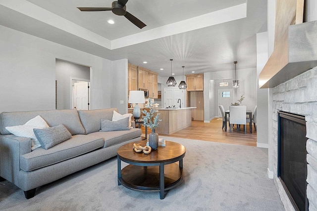 living room featuring ceiling fan with notable chandelier, light wood-type flooring, a fireplace, and sink