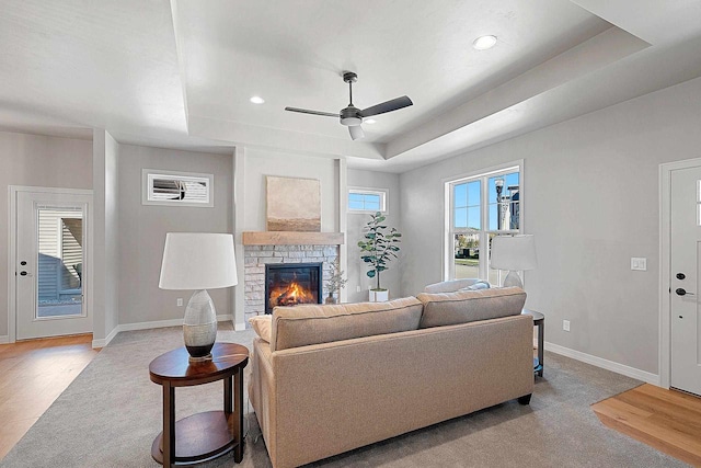 living room with a fireplace, ceiling fan, light hardwood / wood-style flooring, and a raised ceiling