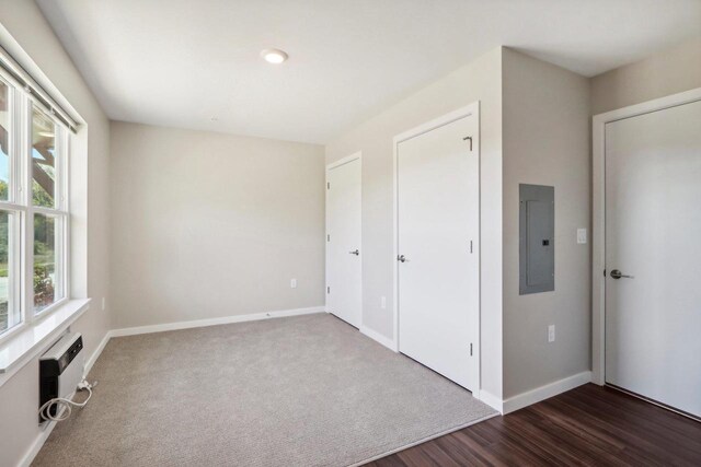 unfurnished bedroom with electric panel, a wall unit AC, and dark hardwood / wood-style floors