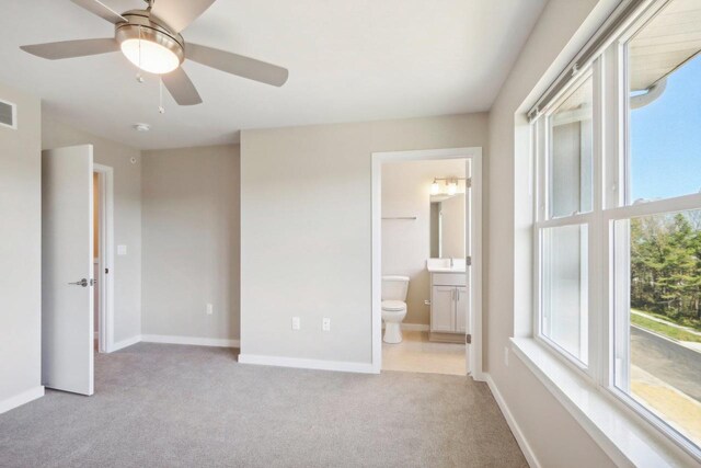 unfurnished bedroom featuring light colored carpet, ensuite bath, and ceiling fan