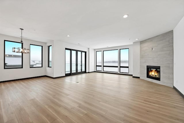 unfurnished living room featuring baseboards, light wood-style floors, a fireplace, a notable chandelier, and recessed lighting