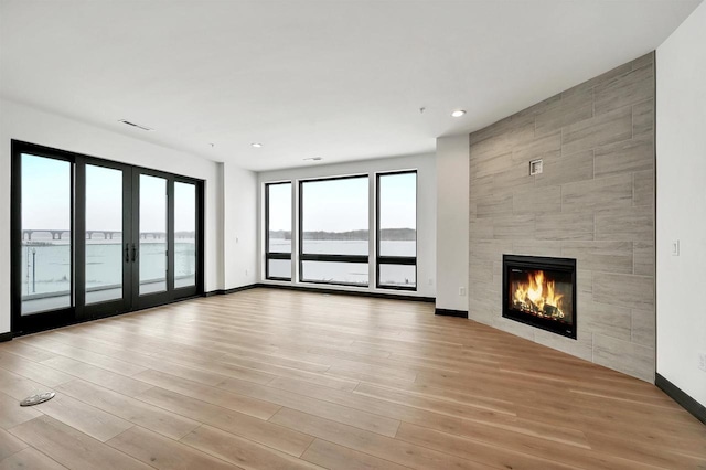 unfurnished living room featuring light wood-style flooring, visible vents, french doors, and a tile fireplace