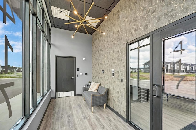 doorway to outside with visible vents, baseboards, wood finished floors, an inviting chandelier, and a high ceiling