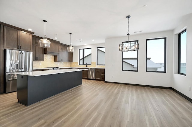 kitchen with dark brown cabinetry, tasteful backsplash, light wood-style flooring, stainless steel appliances, and light countertops