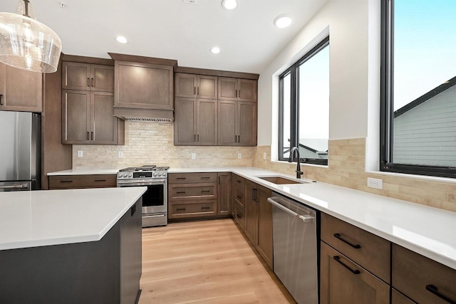 kitchen featuring stainless steel appliances, light countertops, custom range hood, and a sink