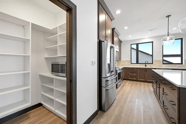 kitchen with stainless steel appliances, light countertops, light wood-style flooring, a sink, and dark brown cabinetry