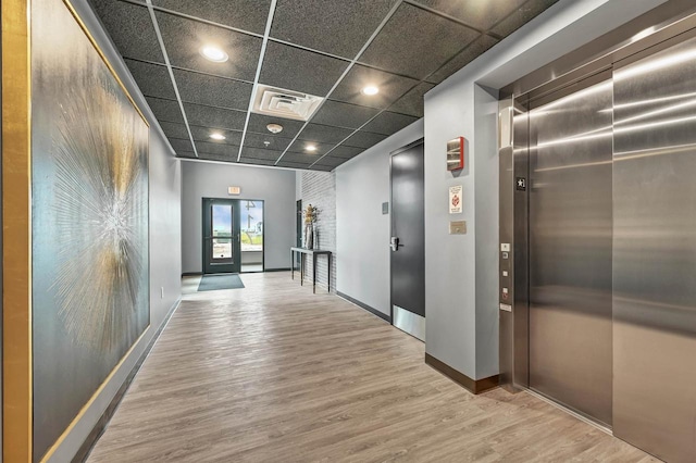 hall with a paneled ceiling, wood finished floors, visible vents, baseboards, and elevator