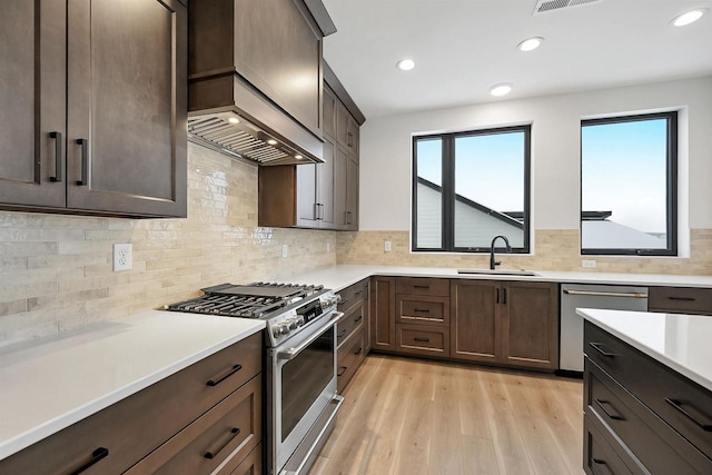 kitchen with custom range hood, stainless steel appliances, dark brown cabinets, light countertops, and a sink