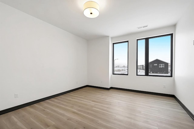 unfurnished room featuring light wood-style floors, visible vents, and baseboards