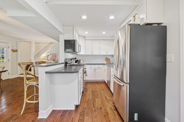 kitchen with white cabinets, a breakfast bar, hardwood / wood-style flooring, kitchen peninsula, and appliances with stainless steel finishes