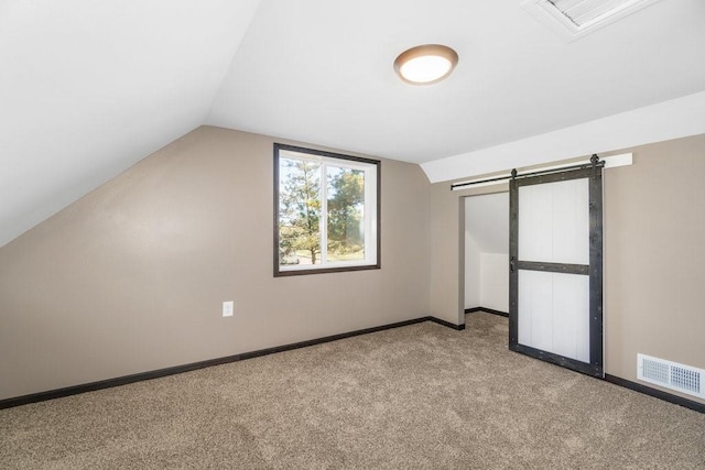 additional living space featuring light carpet, a barn door, and vaulted ceiling