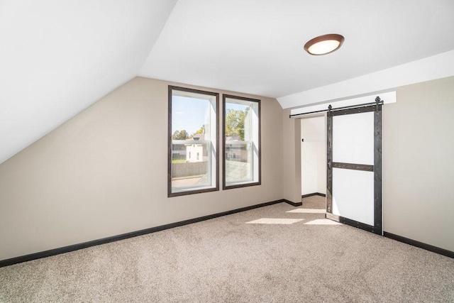 additional living space featuring lofted ceiling, a barn door, and light colored carpet