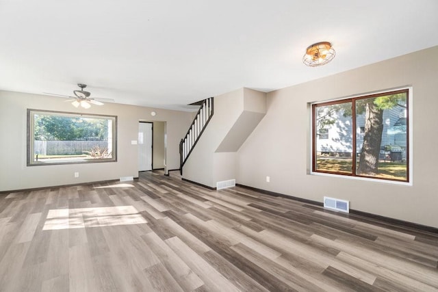 unfurnished living room featuring ceiling fan, light wood-type flooring, and plenty of natural light